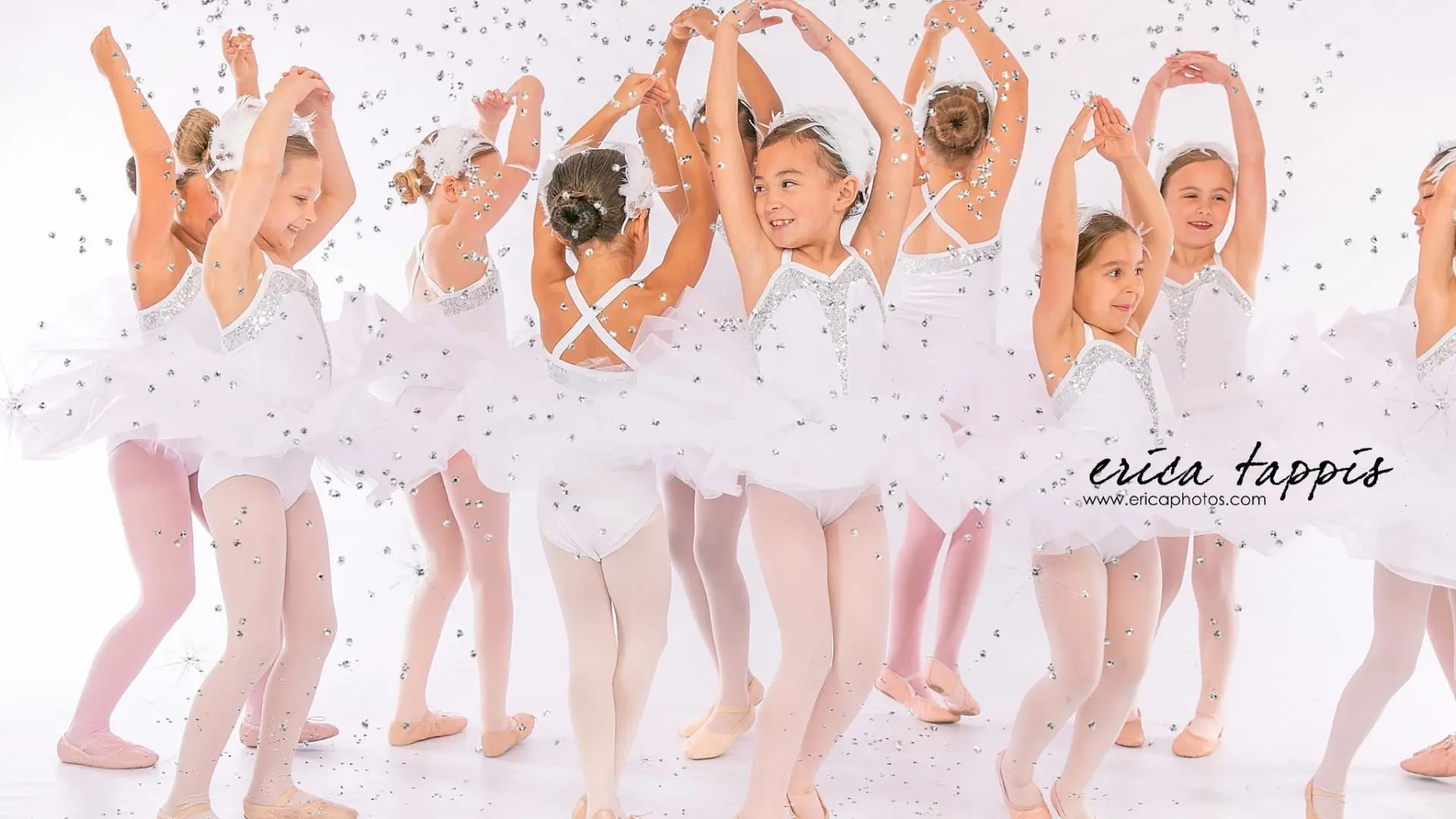 Young ballet dancers in white tutus with arms raised and confetti falling at Bella Ballet